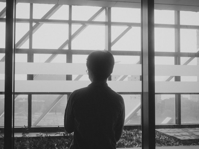 Black-and-white silhouette of a man looking out of a large window