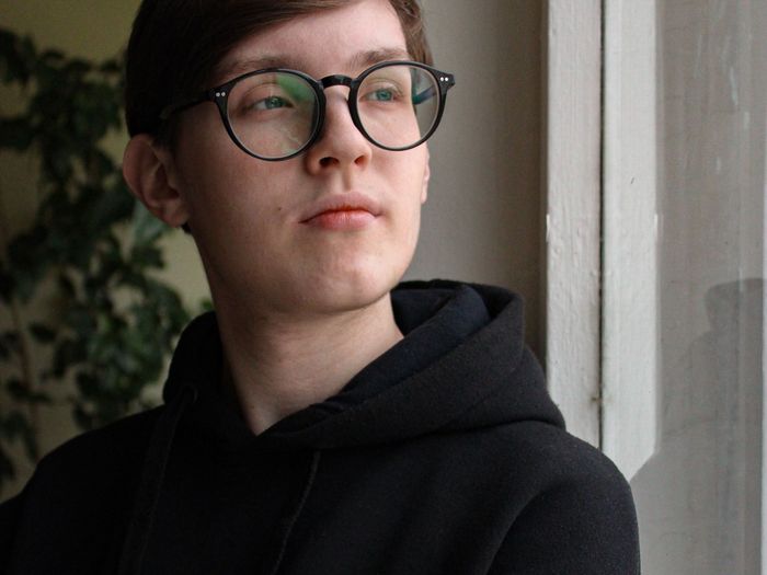 A young man in a black hoodie looking out of a window